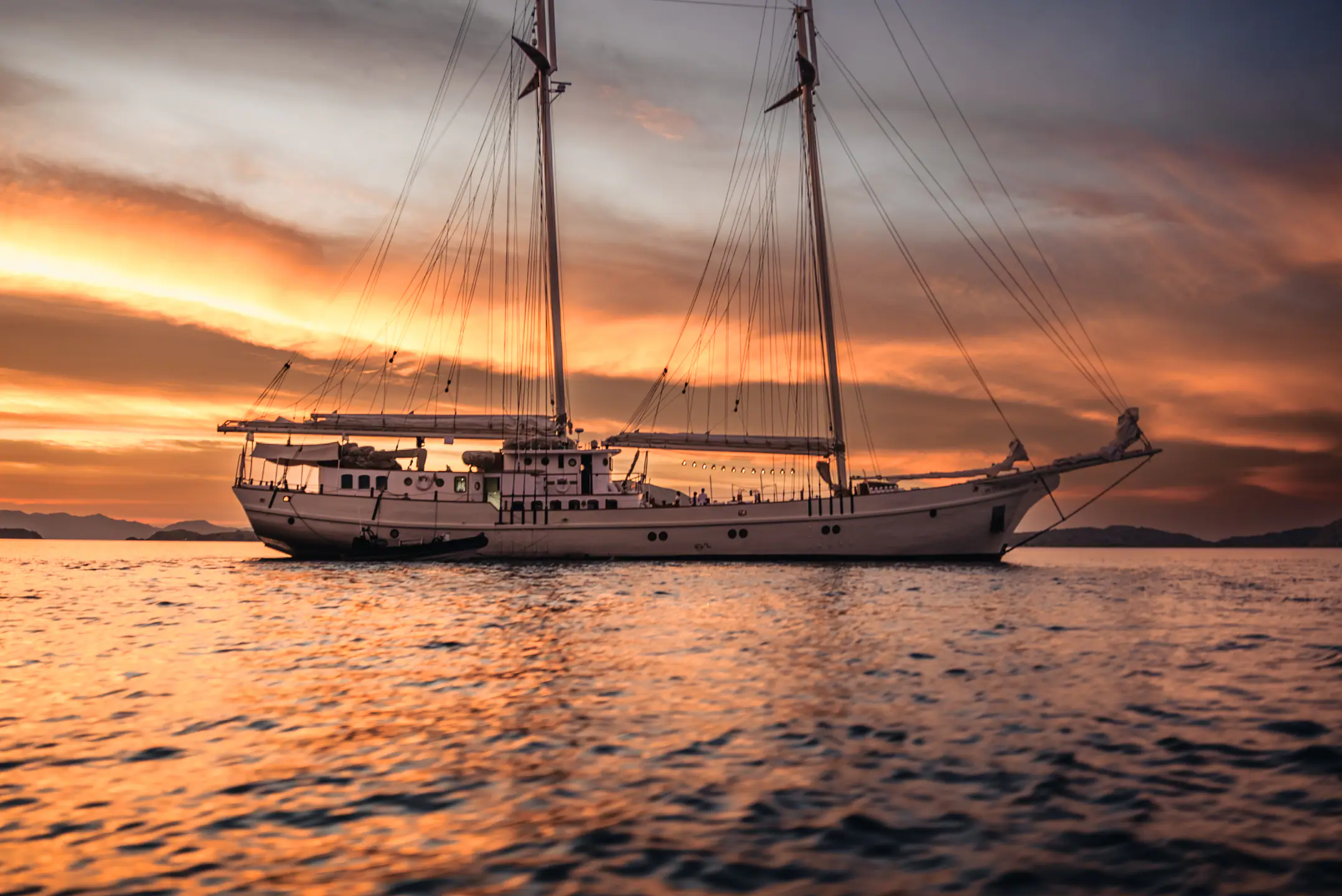 Mutiara Laut schooner yacht sailing at sunset across the Indonesian archipelago.