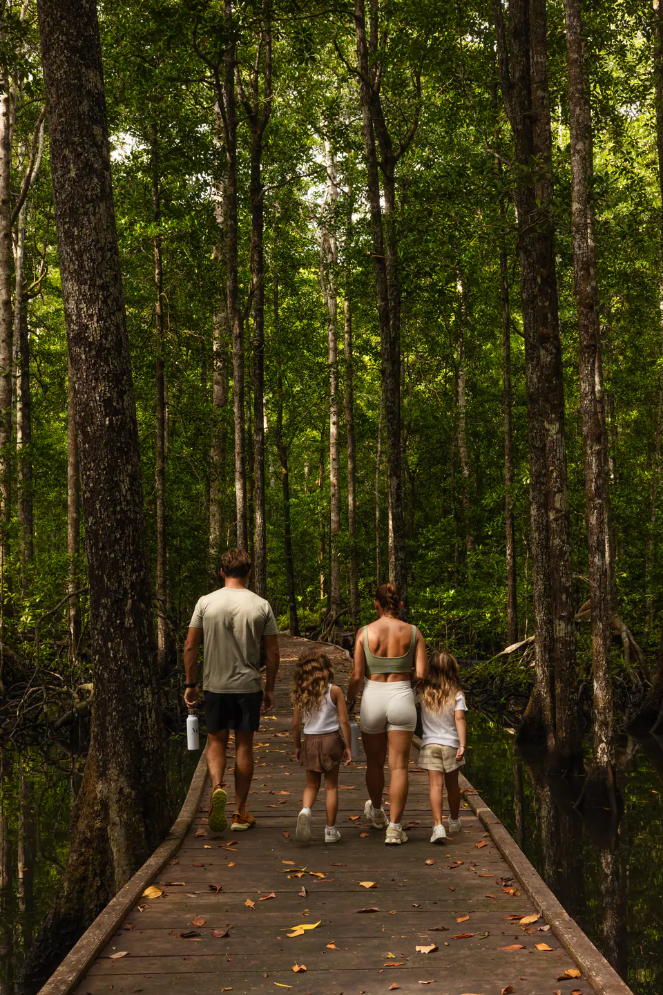 Mutiara Laut guest on a jungle expedition crossing a wooden bridge surrounded by tropical forest.