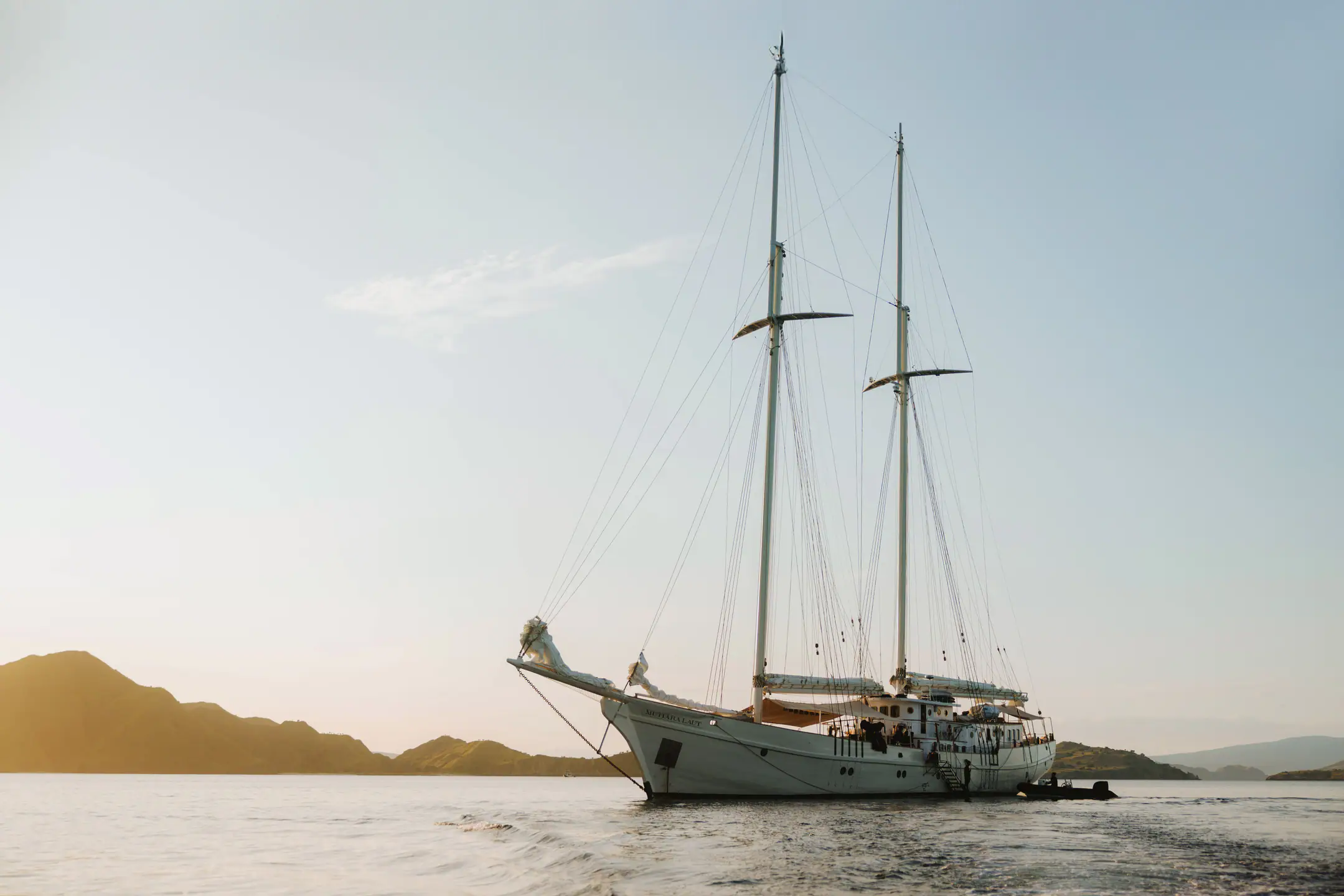 Mutiara Laut sailing yacht drifting across calm seas at golden hour.