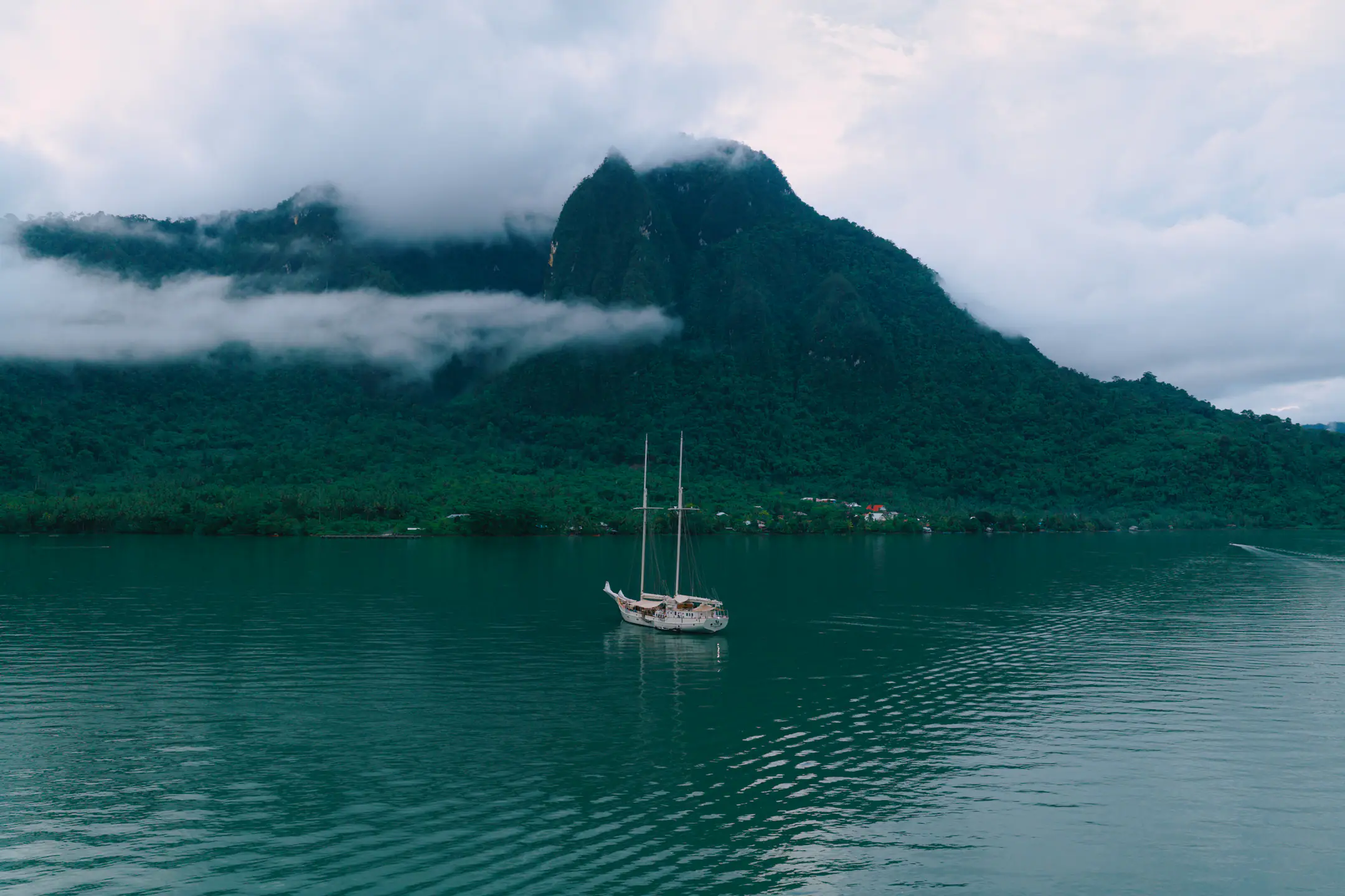 Mutiara Laut anchored in a tranquil bay surrounded by lush tropical mountains.